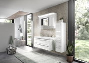 Modern badkamermeubel in een lichte badkamer met grote ramen, bestaande uit een witte wastafel met lades en een hoge, smalle kast. Aanzicht van schuin van voren.