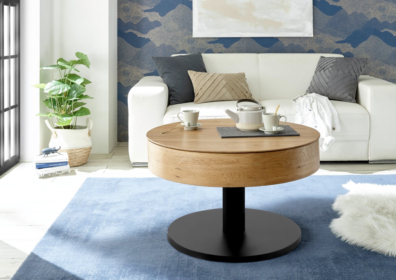Ronde houten salontafel met zwarte voet, in de woonkamer met bank en decoraties, zijaanzicht.