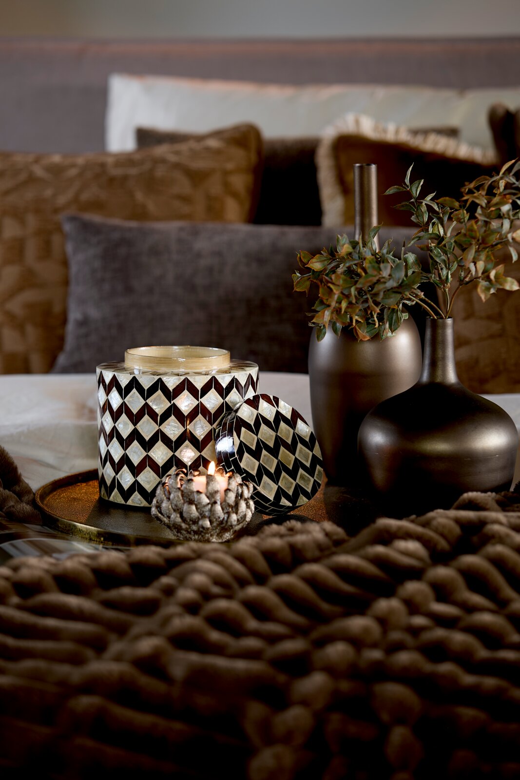 Vooraanzicht van een luxe cilindervormige kaarsenhouder met zwart-wit ruitmozaïek en afneembaar deksel, sfeervol gestyled met brandende kaars en donkere vazen.