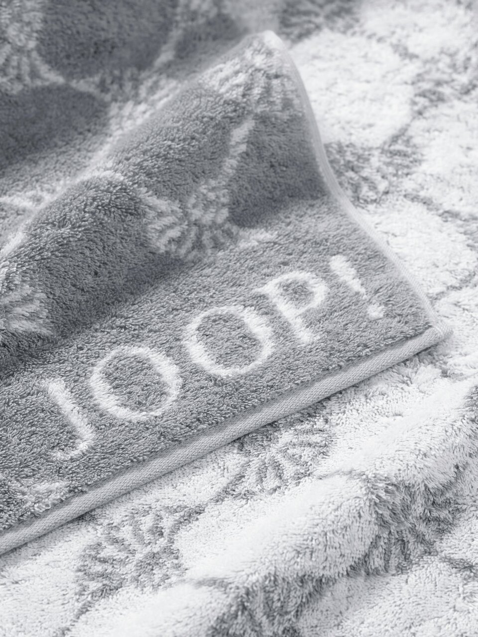 JOOP! Handtuch CORNFLOWER CLASSIC Graues Handtuch mit eingewebtem Muster und dem Schriftzug 'JOOP!' in Nahaufnahme.