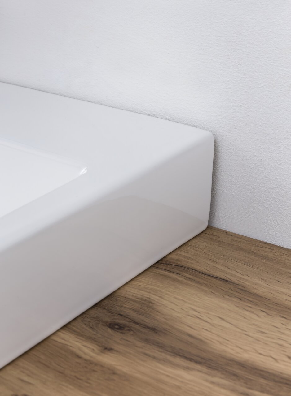 Close-up van een witte wastafel op een houten ondergrond, gezien vanaf de zijkant.