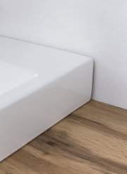 Close-up van een witte wastafel op een houten ondergrond, gezien vanaf de zijkant.
