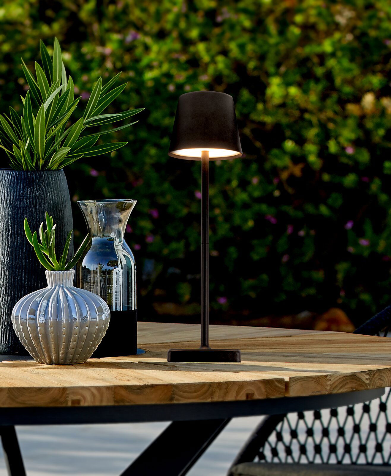 Elegante Solarleuchte auf einem Holztisch im Freien, umgeben von dekorativen Vasen und Pflanzen, seitliche Perspektive.