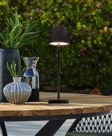 Elegante Solarleuchte auf einem Holztisch im Freien, umgeben von dekorativen Vasen und Pflanzen, seitliche Perspektive.