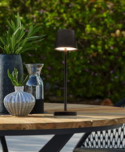 Elegante Solarleuchte auf einem Holztisch im Freien, umgeben von dekorativen Vasen und Pflanzen, seitliche Perspektive.