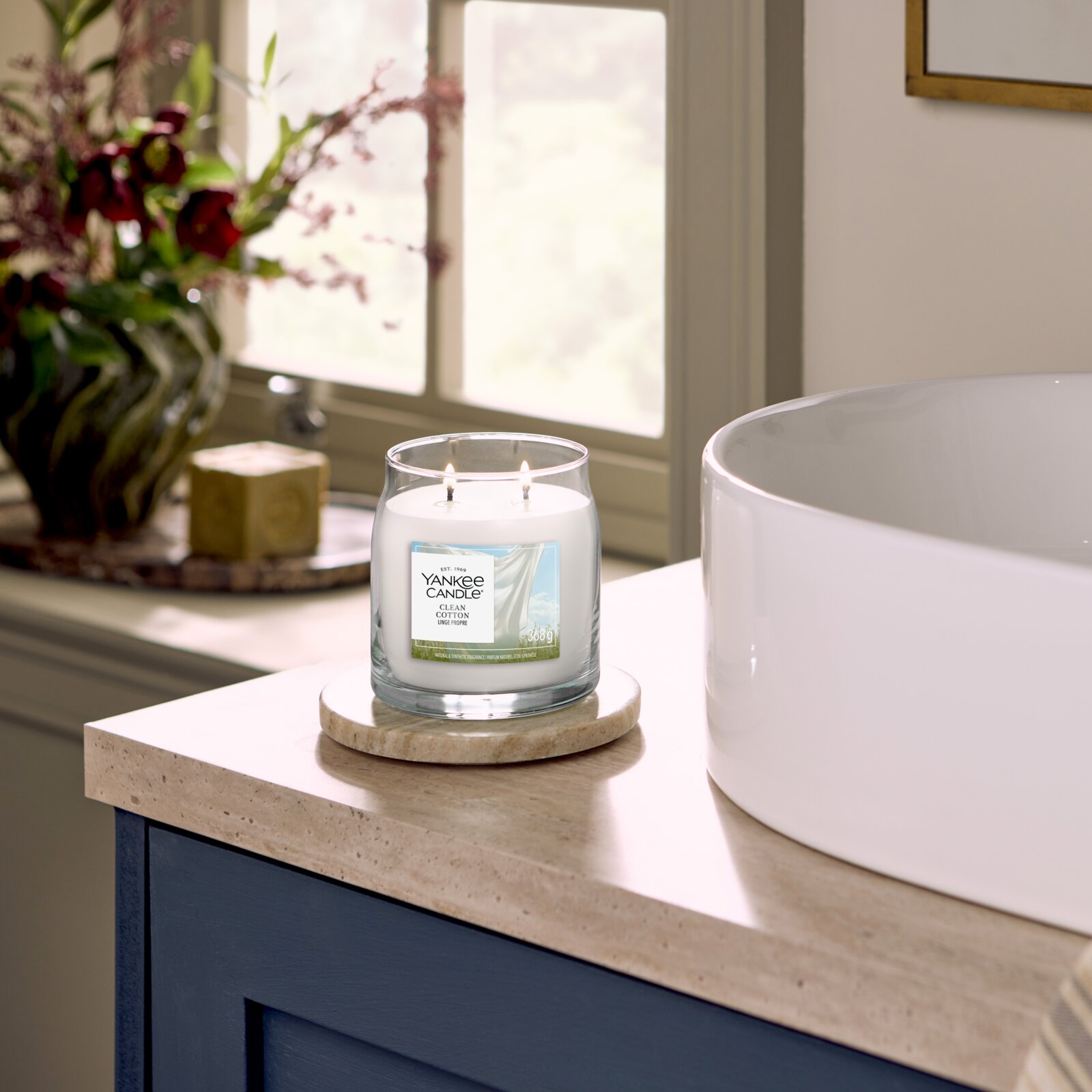 Brandende Yankee Candle Clean Cotton geurkaars met twee lonten in een glazen pot van 368 g, vanuit schuin vooraanzicht naast een vrijstaand bad