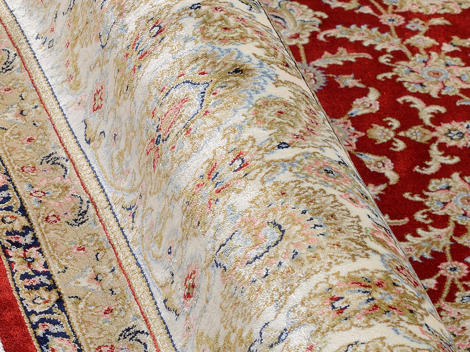 Nahaufnahme eines Orientteppichs mit floralem Muster in Rot, Beige und Blau, teilweise aufgerollt.