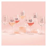 Eine Sammlung von Weingläsern mit humorvollen Sprüchen, gefüllt mit Roséwein, auf einem rosa Hintergrund. Frontale Perspektive.