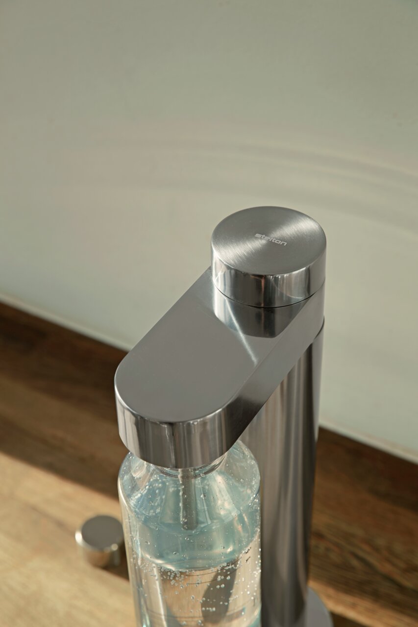 Close-up van een Brus-soda-maker van roestvrij staal met een aangesloten fles, gezien van bovenaf.