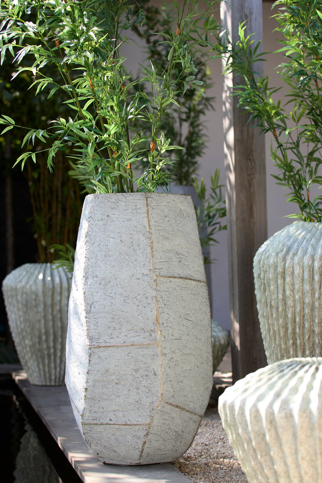 Light&Living Topf AGELO 88cm Großer, moderner Pflanztopf aus Beton mit geometrischem Design, gefüllt mit grünen Pflanzen, in einer Außenumgebung. Perspektive von vorne.