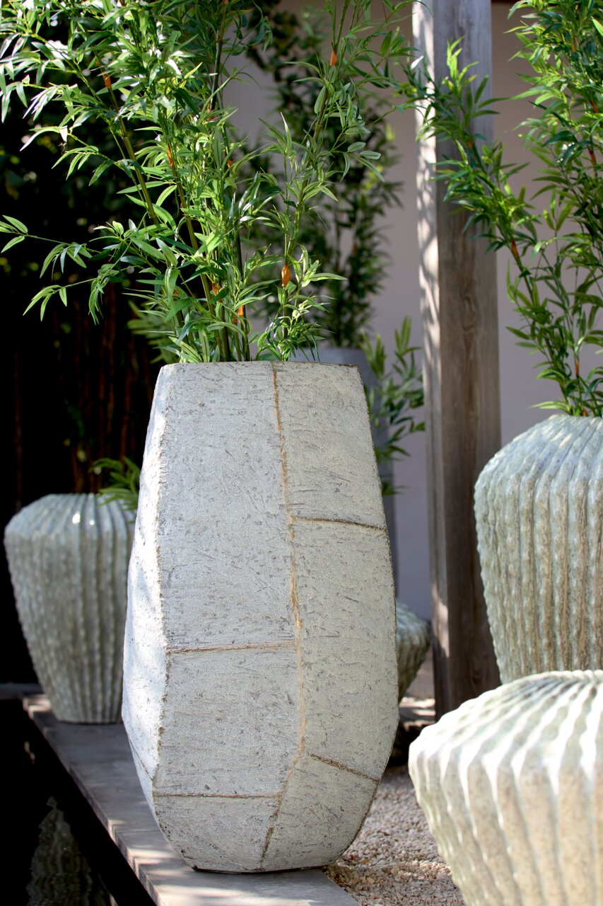 Light&Living Pan AGELO 88 cm Grote, moderne betonnen plantenpot met een geometrisch ontwerp, gevuld met groene planten, in een buitenomgeving. Vooraanzicht.