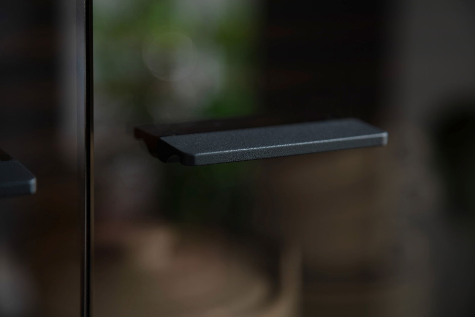Nahaufnahme eines schwarzen Griffs an einer Glastür, seitliche Perspektive.