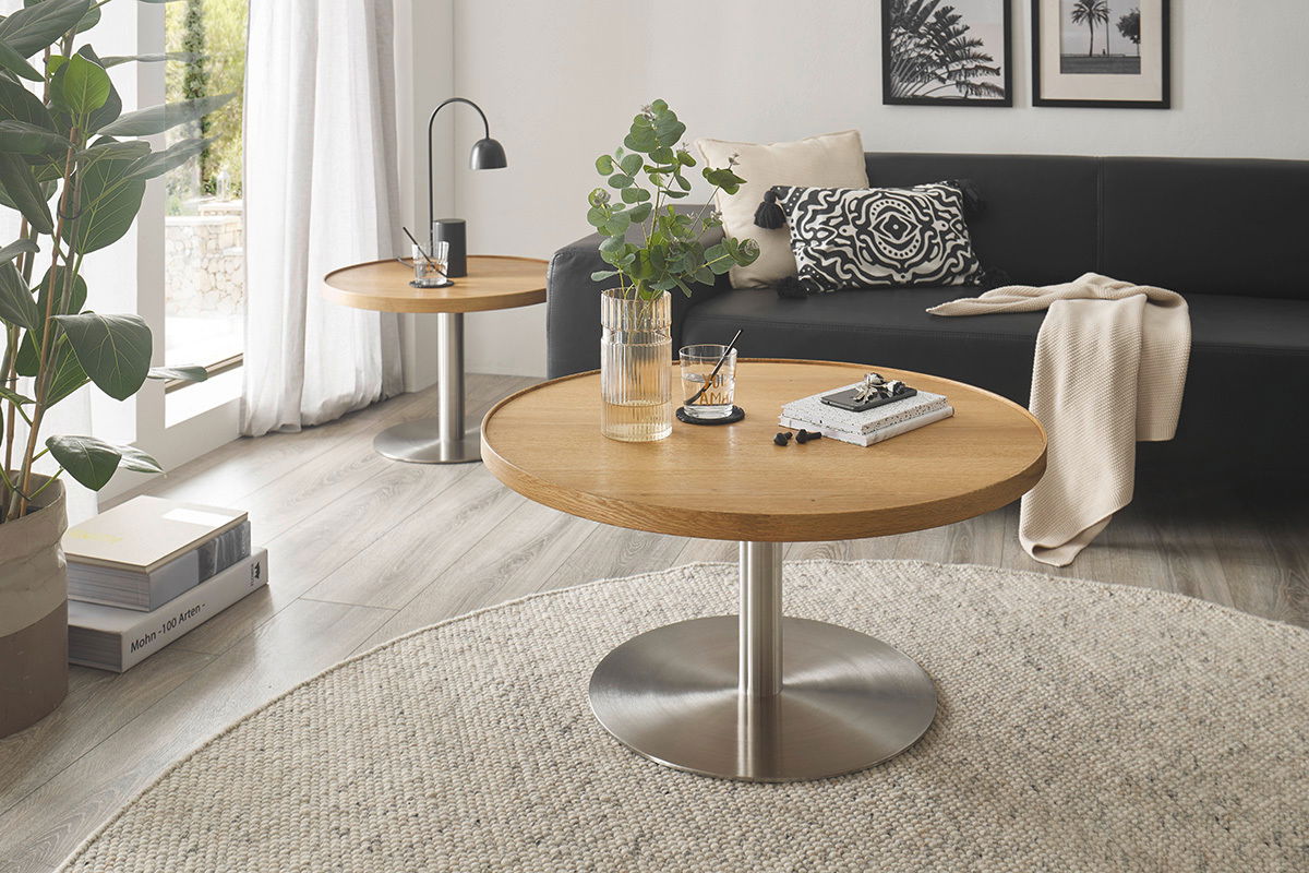 Runder Couchtisch mit Holzplatte und Metallfuß, im Wohnzimmer mit Sofa und Dekorationen, aus seitlicher Perspektive.