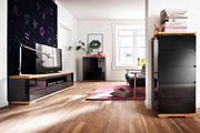 Modernes Wohnzimmer mit TV-Lowboard, Hochkommode und Highboard in schwarzem Hochglanz und Holzoptik, seitliche Perspektive.