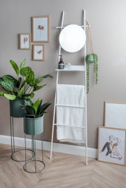 Ein modernes Pflanzgefäß-Set bestehend aus drei Teilen, präsentiert in einem stilvollen Innenraum. Zwei Pflanzen stehen in eleganten, grünen Töpfen auf Metallständern. Perspektive: Frontalansicht.