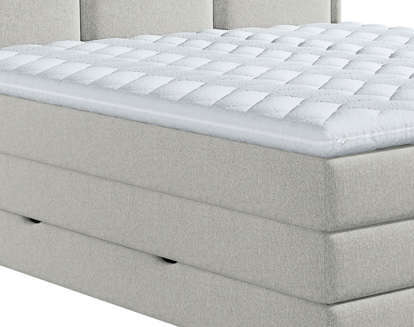 Witte, dik gewatteerde matrastopper met doorgestikt patroon en ritssluiting op een lichtgrijs gestoffeerd boxspringbed, schuin van voren en bovenaf gezien