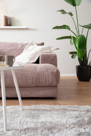 Großes Megasofa in einem modernen Wohnzimmer, seitliche Perspektive mit Kissen, Beistelltisch und Zimmerpflanze.