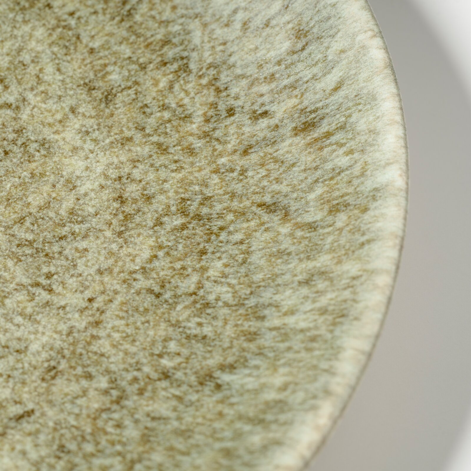 Detailaufnahme einer runden Naturstein- oder Marmorplatte in Beige mit brauner Maserung, schräg von oben fotografiert