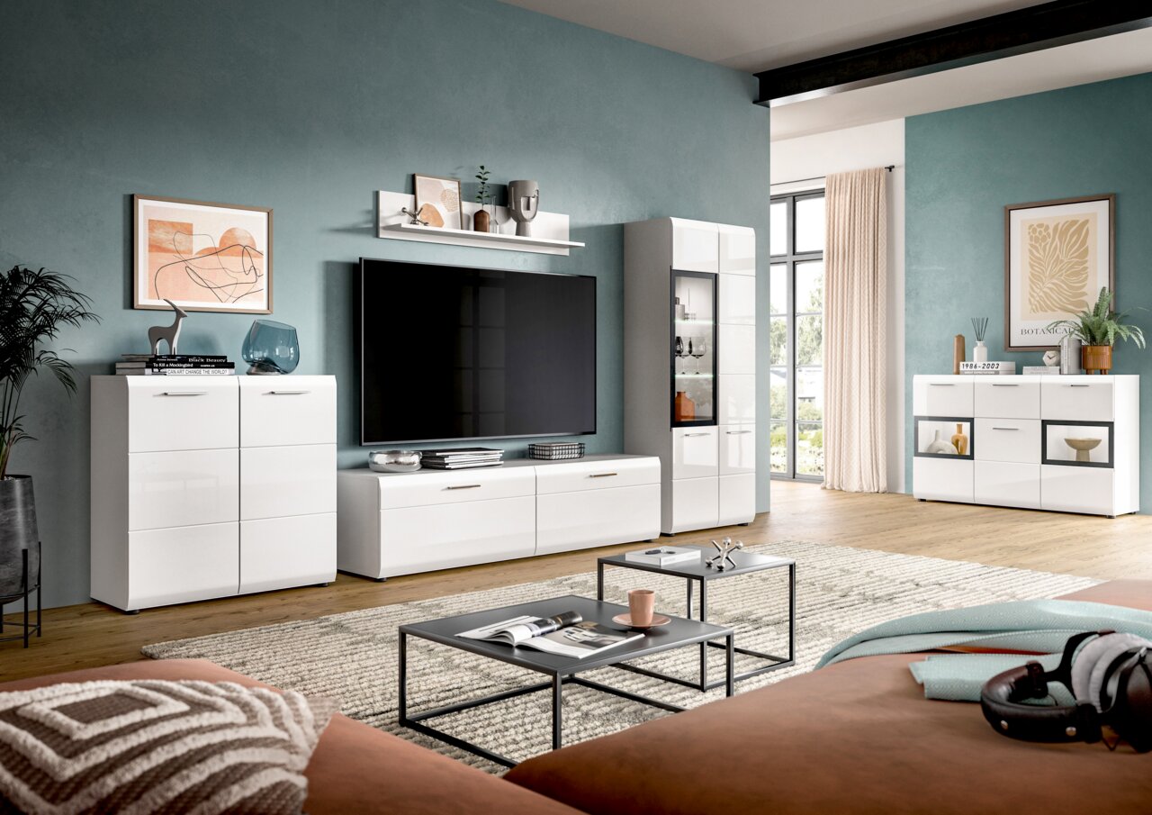 Modernes Wohnzimmer mit weißer, hochglänzender Wohnwand (Lowboard, Vitrine, Sideboards und Wandregal) vor petrolfarbener Wand, TV mittig, aufgenommen in frontaler Perspektive mit leichter Weitwinkelansicht.