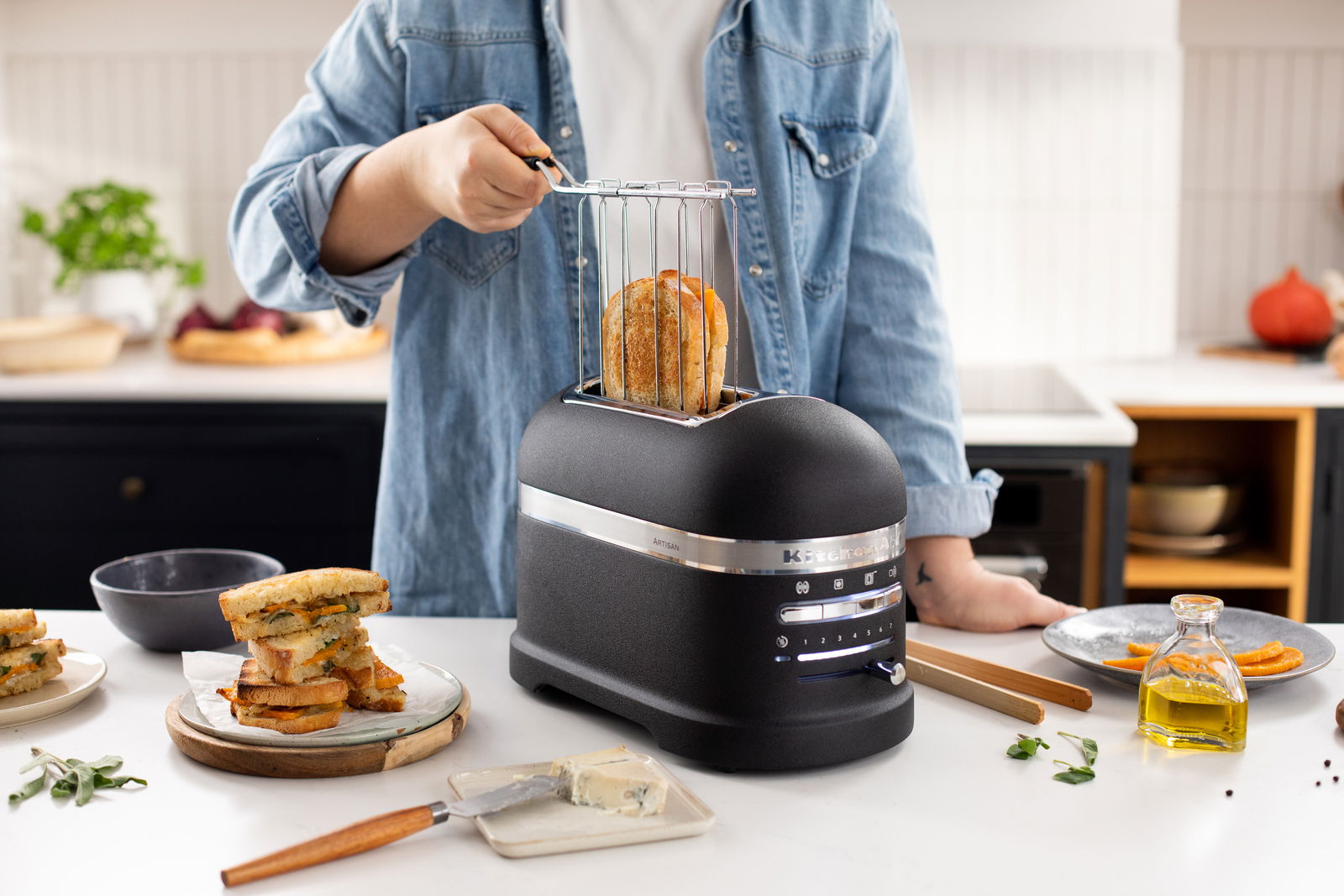 Schwarzer 2-er Toaster aus Guss auf einer Küchenarbeitsplatte, mit einer Person, die Brot mit einem Brötchenaufsatz toastet. Perspektive von vorne.