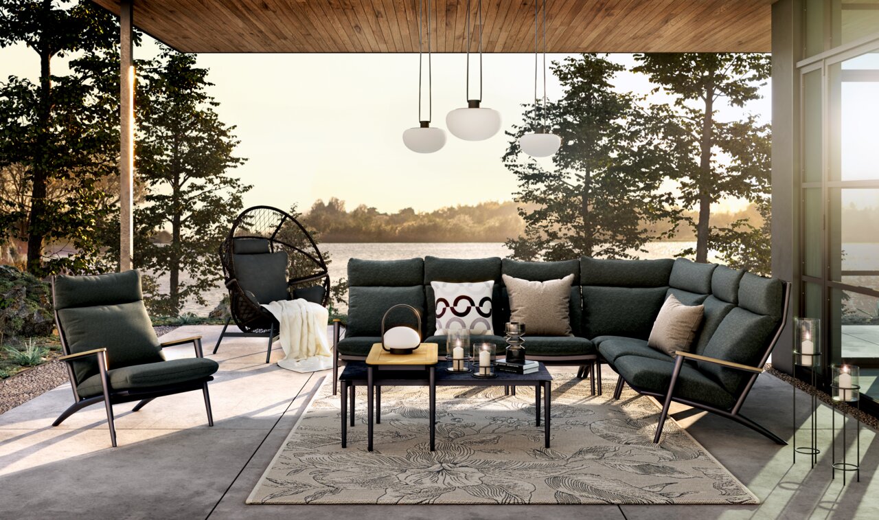 Moderne Loungegarnitur mit dunkelgrünen Polstern und eleganten Metallrahmen, umgeben von einem natürlichen Außenbereich mit Seeblick, aus der Frontalperspektive.