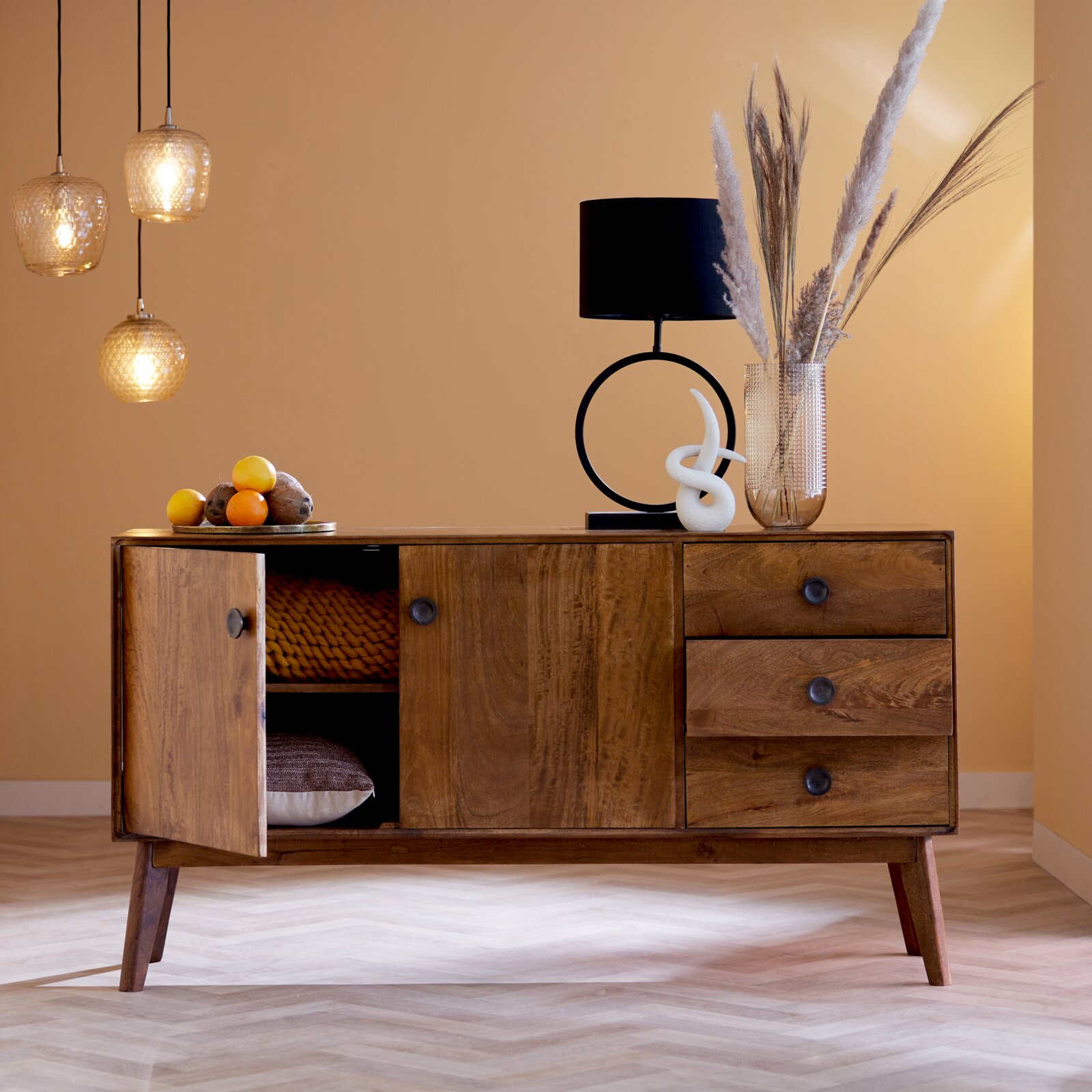 Moderner Wohnraum mit einem hölzernen Sideboard, auf dem ein schwarzer Lampenschirm in Zylinderform steht. Die Perspektive zeigt das Sideboard von vorne, mit dekorativen Elementen wie einer Vase und einer Skulptur daneben.