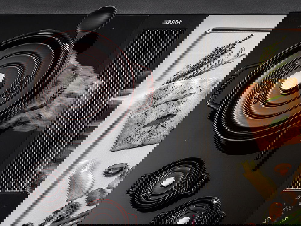 Moderne Kücheneinrichtung mit Dampfkochtopf, elegantem Induktionskochfeld und gekochtem Kräuterfisch auf einer Edelstahlplatte.