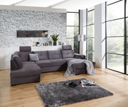 Graues Ecksofa in modernem Wohnzimmer mit großen Fenstern, von vorne betrachtet.