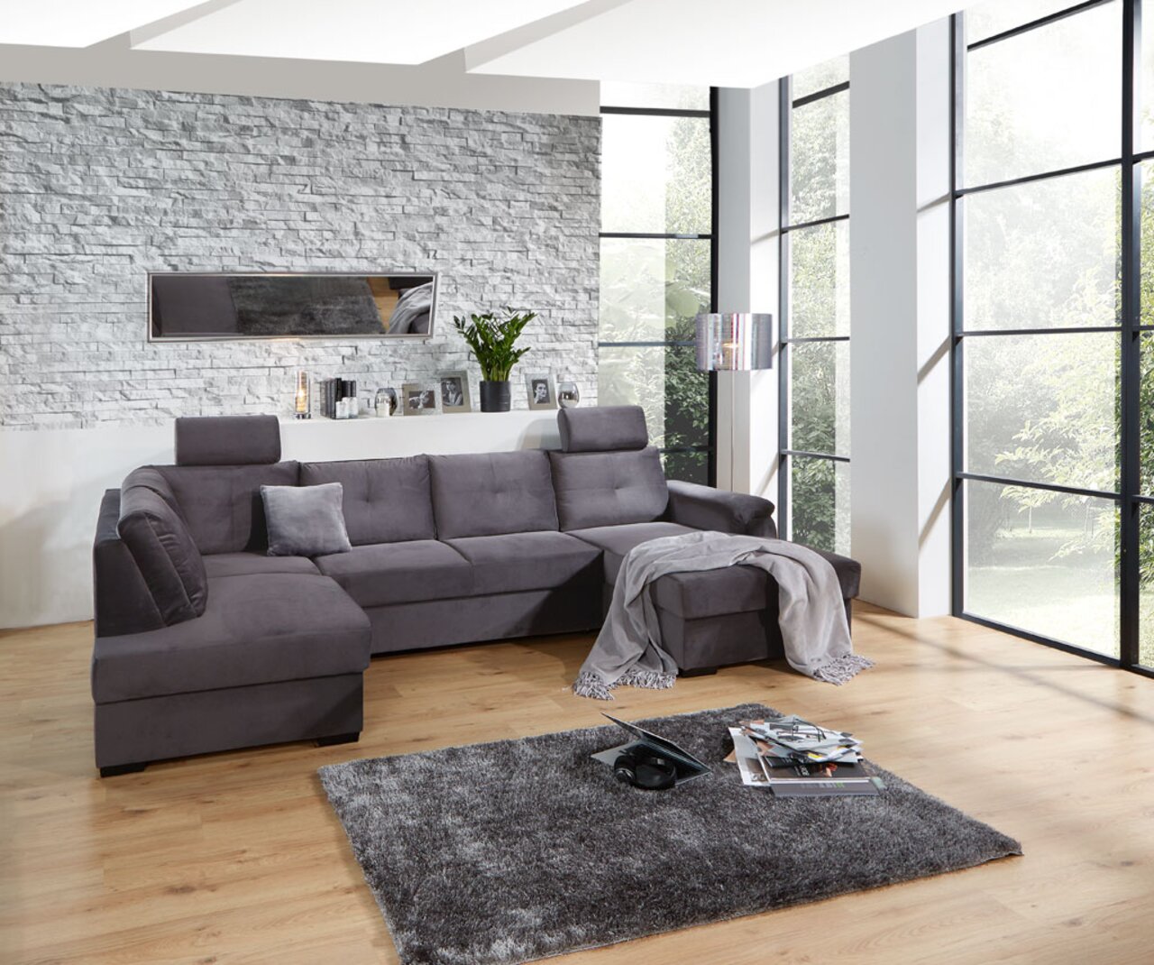 Graues Ecksofa in modernem Wohnzimmer mit großen Fenstern, von vorne betrachtet.