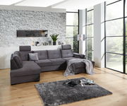 Graues Ecksofa in modernem Wohnzimmer mit großen Fenstern, von vorne betrachtet.