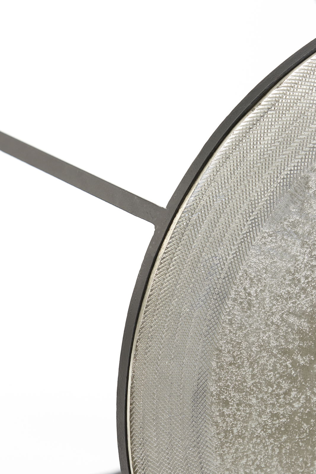 Nahaufnahme eines runden Beistelltisches mit strukturiertem Metallrahmen und glatter Oberfläche, seitliche Perspektive.
