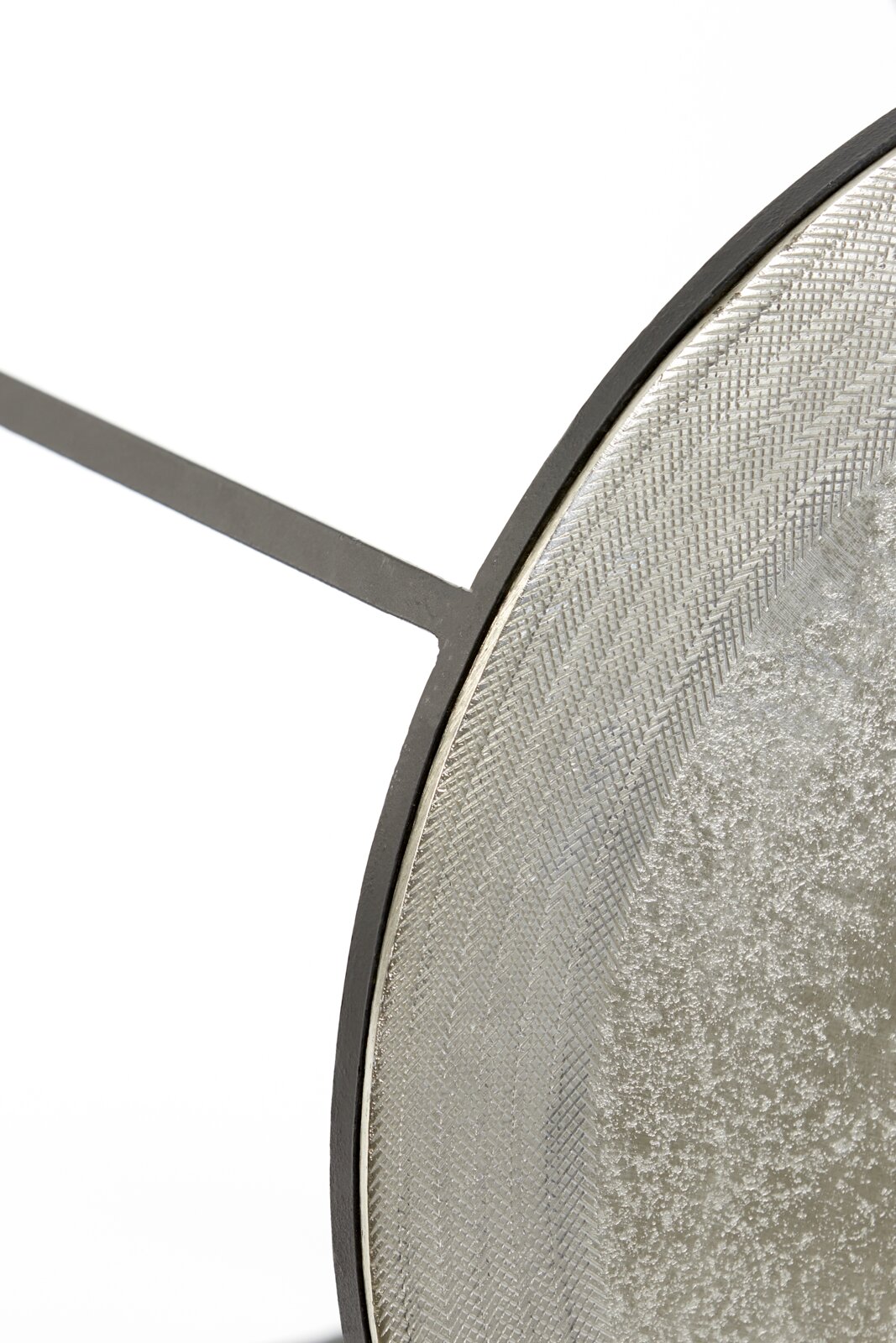 Close-up van een rond bijzettafeltje met een gestructureerd metalen frame en een glad oppervlak, gezien vanaf de zijkant.