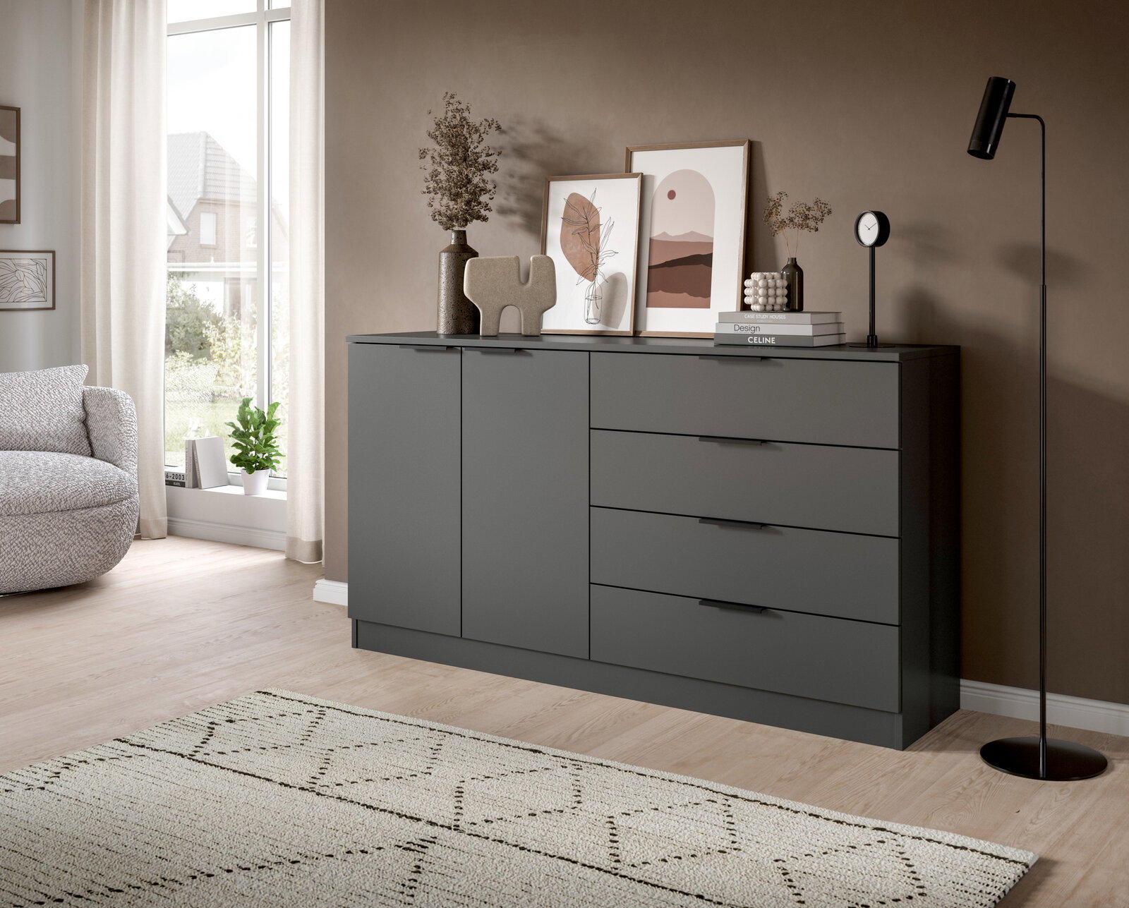 Moderne dunkelgraue Kommode mit zwei Türen und vier Schubladen, dekoriert mit Bildern, Vasen und Büchern, im Wohnzimmer – Perspektive: frontale Ansicht leicht von links.