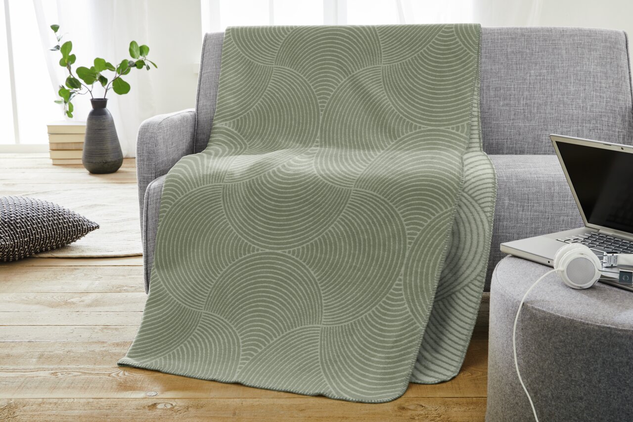 Bugatti Decke150x200cm BUGATTI Graue Jacquard Decke mit kreisförmigem Muster auf einem Sofa drapiert, seitliche Perspektive