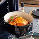 Gusseiserner ovaler Bräter mit gebratenem Hähnchen und Knoblauch, im Ofen auf einem Rost von schräg oben fotografiert.