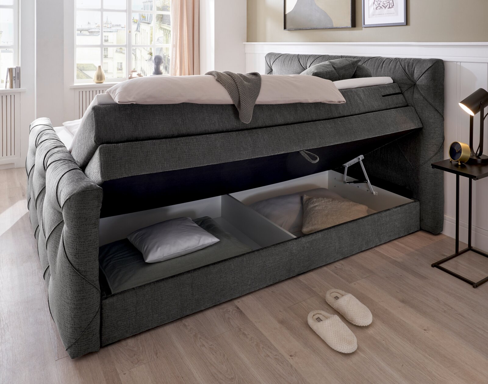 Boxspringbed met open opbergruimte, zijaanzicht, grijze stoffen bekleding, lichte omgeving