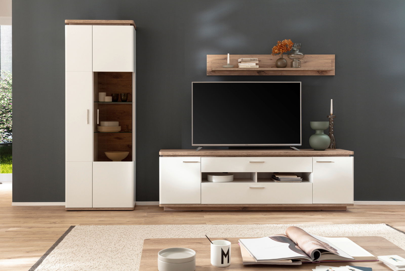 Moderne Wandkombination in hellem Holz und Weiß, bestehend aus einem hohen Schrank, einem TV-Board und einem Wandregal, frontal betrachtet.