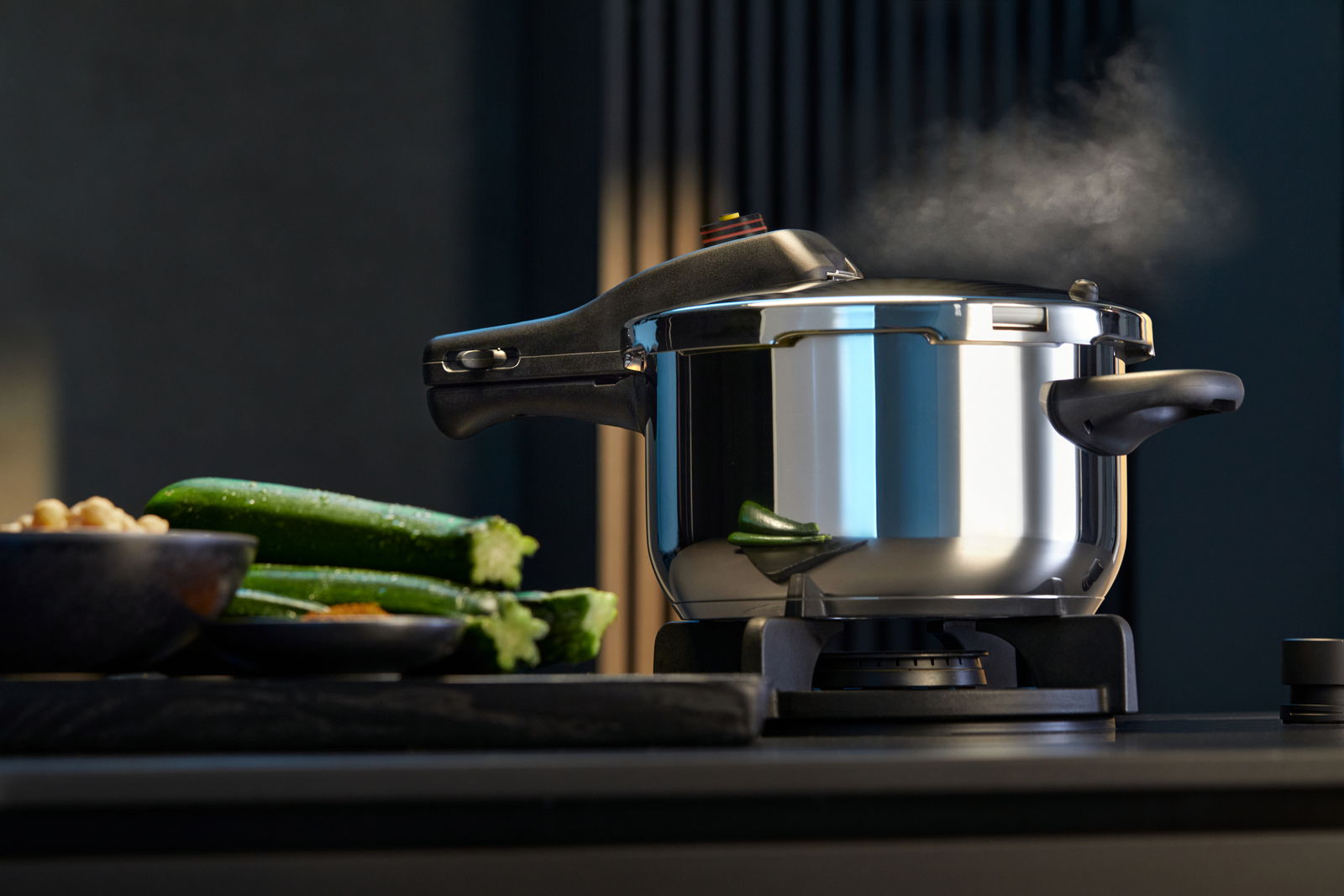 Schnellkochtopf PERFECT NEU 4,5L auf einem Herd, seitliche Perspektive, mit Dampf und frischem Gemüse im Vordergrund.