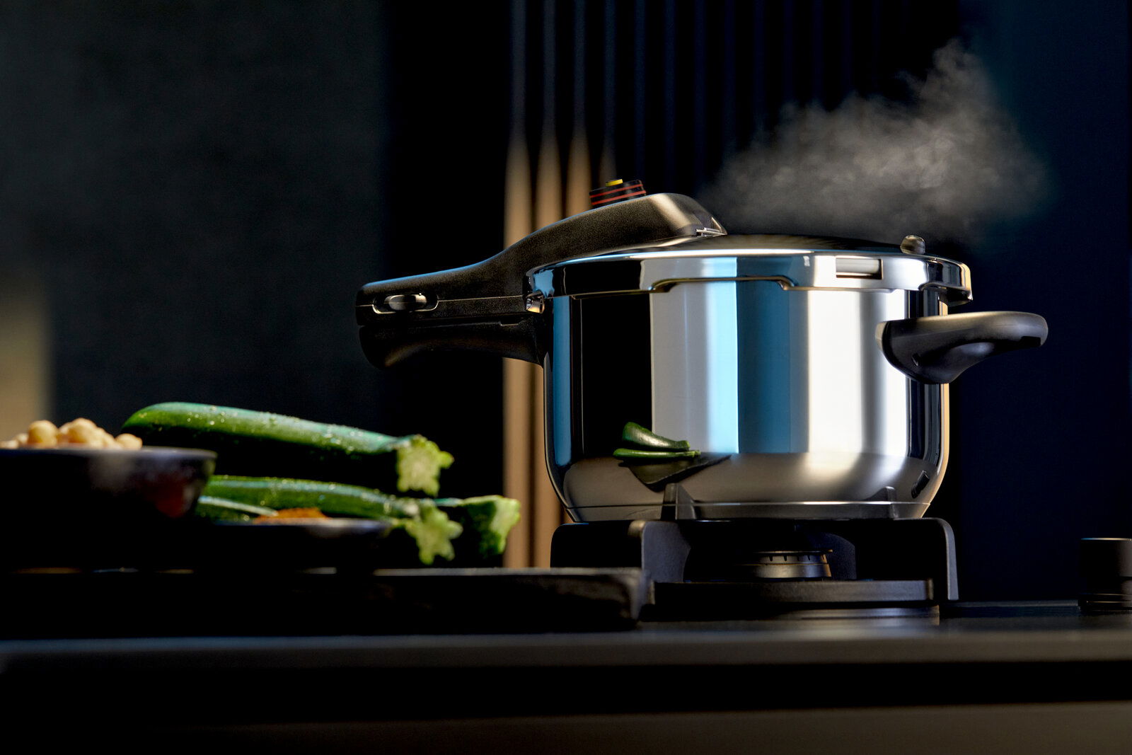 Schnellkochtopf PERFECT NEU 4,5L auf einem Herd, seitliche Perspektive, mit Dampf und frischem Gemüse im Vordergrund.