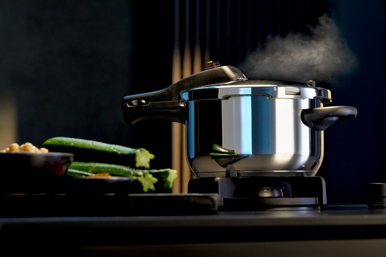Schnellkochtopf PERFECT NEU 4,5L auf einem Herd, seitliche Perspektive, mit Dampf und frischem Gemüse im Vordergrund.
