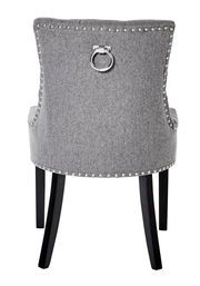 Rückansicht eines grauen Stuhls mit Nietenverzierung und einem dekorativen Metallring an der Rückenlehne, schwarze Beine.