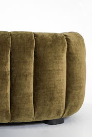Nahaufnahme einer olivgrünen Couch mit weichem, gepolstertem Stoff und vertikalen Nähten, seitliche Perspektive