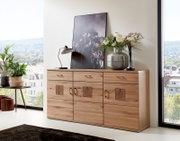 Houten dressoir met drie lades en decoratieve elementen, met daarop een lamp, een schilderij en een vaas met bloemen, gezien vanuit de zijkant.