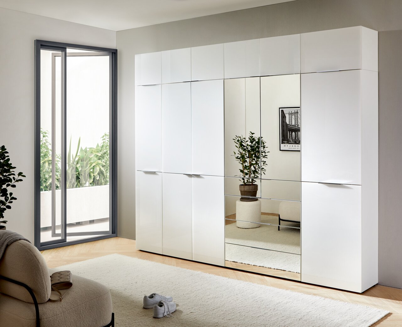 Moderner weißer Stauraumschrank mit Spiegeltüren, seitliche Perspektive, in einem hellen Raum mit Pflanzen und Möbeln.