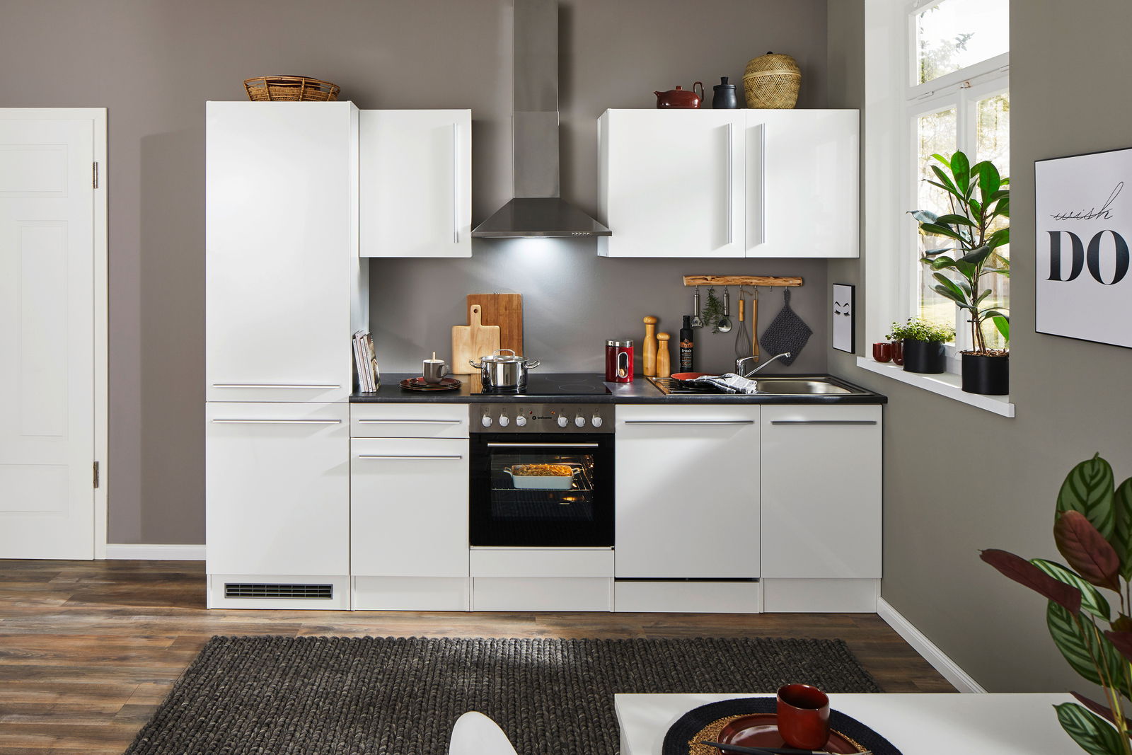 Moderne weiße Küchenzeile mit Herd, Dunstabzugshaube und Spüle, frontal fotografiert.