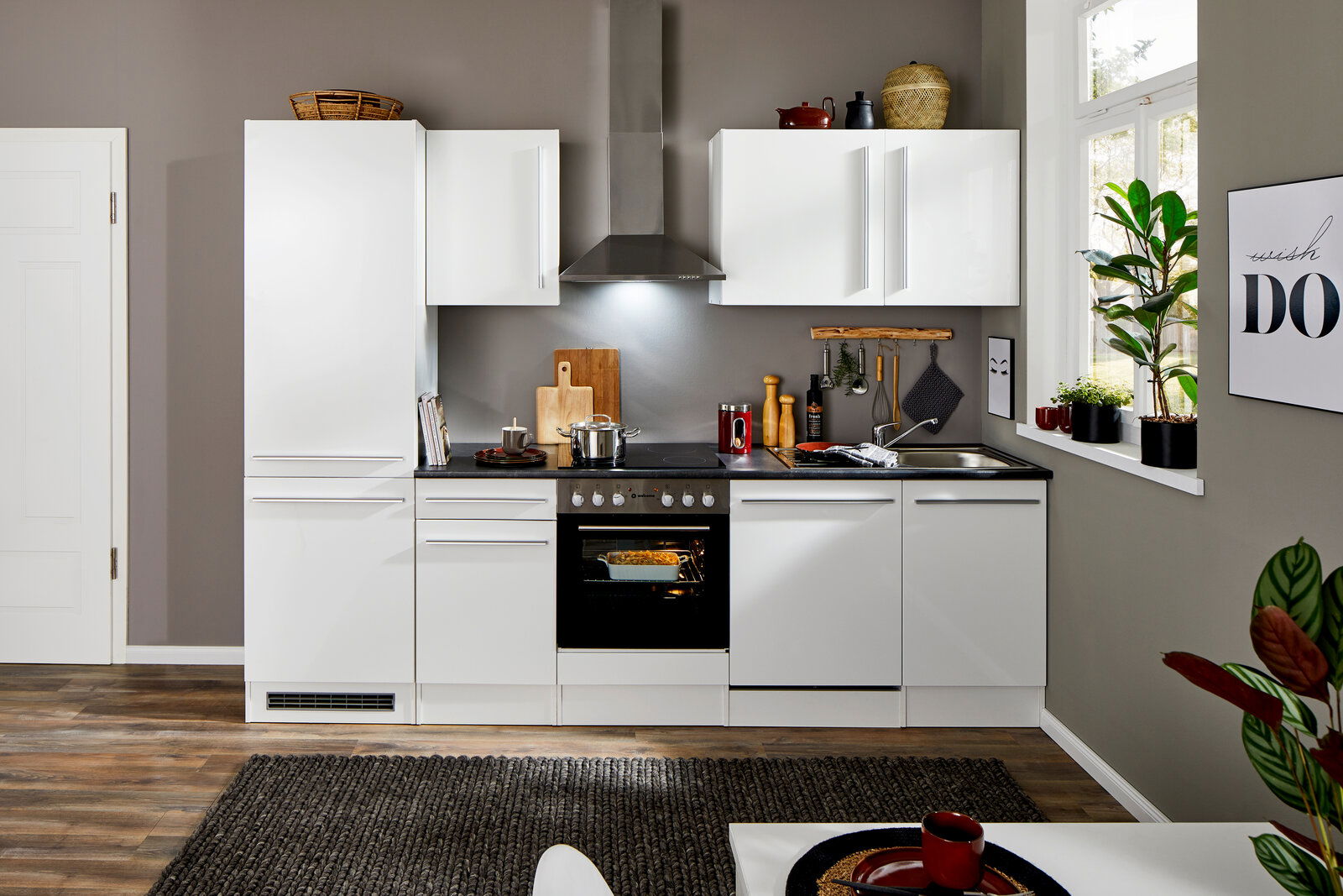 Moderne weiße Küchenzeile mit Herd, Dunstabzugshaube und Spüle, frontal fotografiert.