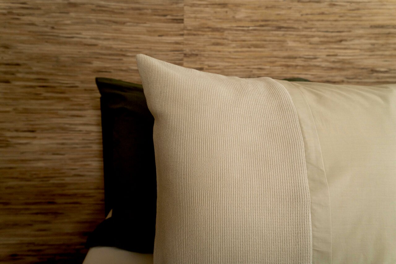 Nahaufnahme von Bettwäsche in Beige und Olivgrün vor einer Holzwand.