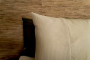 Close-up van beddengoed in beige en olijfgroen tegen een houten wand.