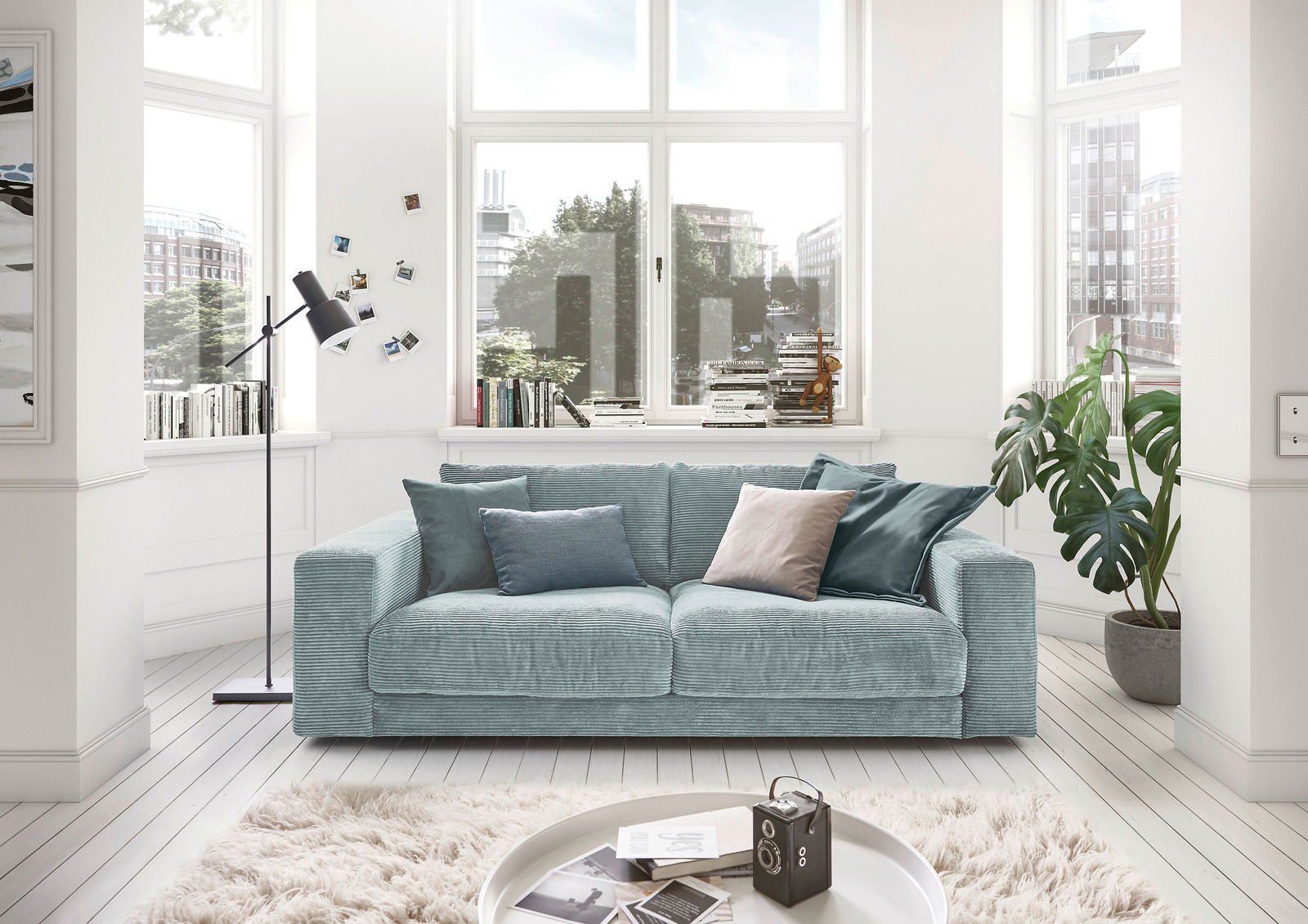Zweiersofa in einem hellen Wohnzimmer mit großen Fenstern, dekoriert mit Kissen in verschiedenen Blautönen, aus der Frontalperspektive.