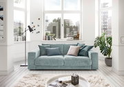 Zweiersofa in einem hellen Wohnzimmer mit großen Fenstern, dekoriert mit Kissen in verschiedenen Blautönen, aus der Frontalperspektive.